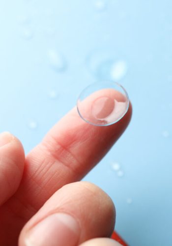 Female hand holds contact lens on blue background, close up